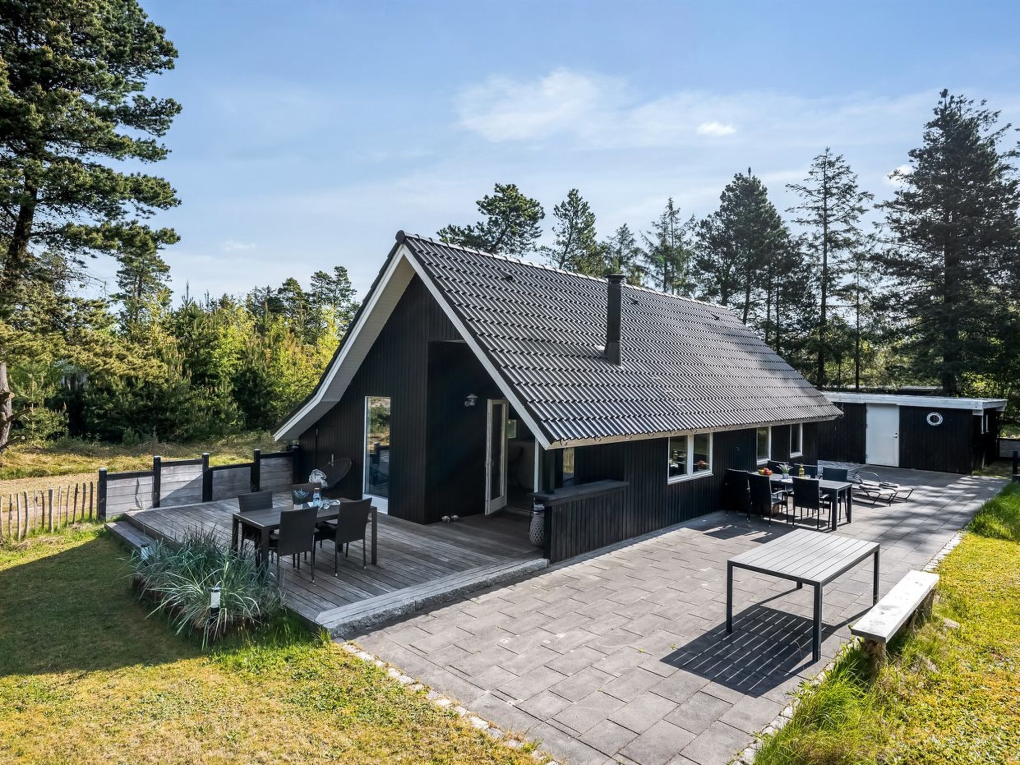 Une cabane moderne dotée d’un toit en pente, d’une terrasse et d’un petit garage attenant.