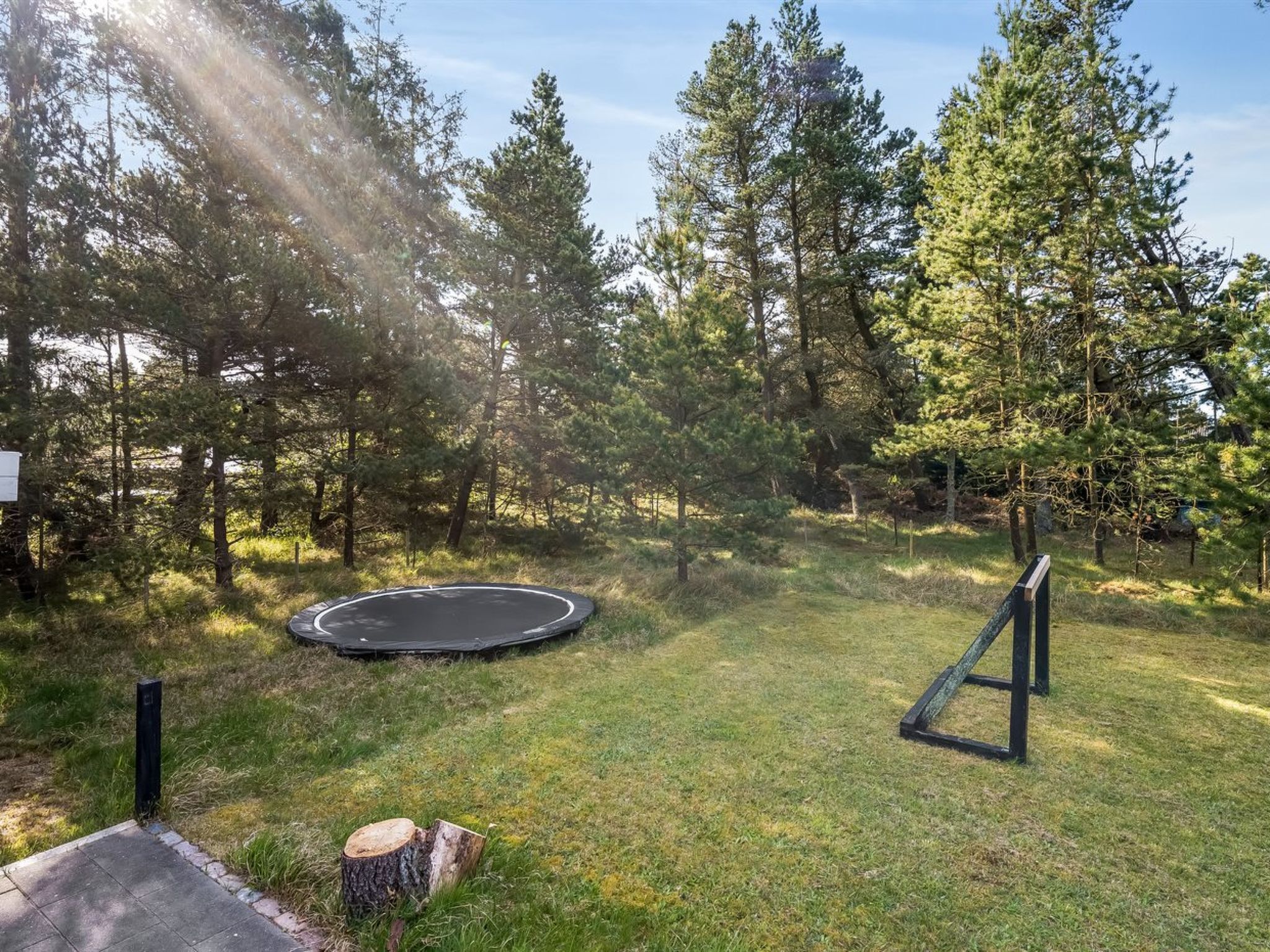 A grassy outdoor area with a trampoline and a wooden structure.