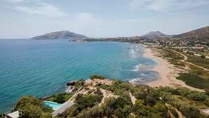 Un complejo turístico frente al mar con piscina, acceso a la playa y montañas al fondo.