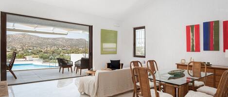 A spacious living area with a pool view, a dining table with wicker chairs, and a large window.