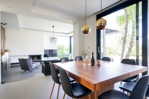 A modern dining area with a wooden table, black chairs, and hanging gold pendant lights. - Filerimos Panorama Villa (Pastida)