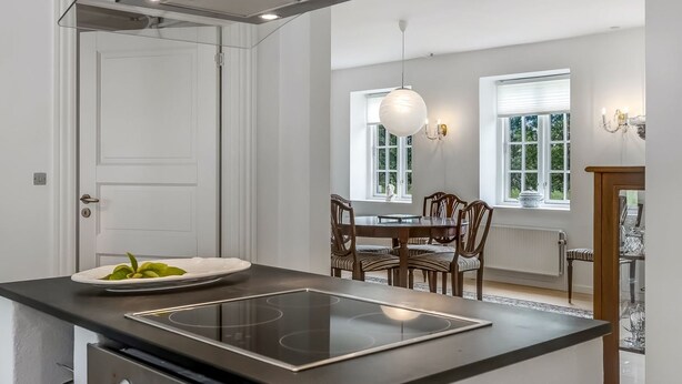 A modern kitchen with a built-in stovetop, a dining area with a table and chairs, and a pendant light.