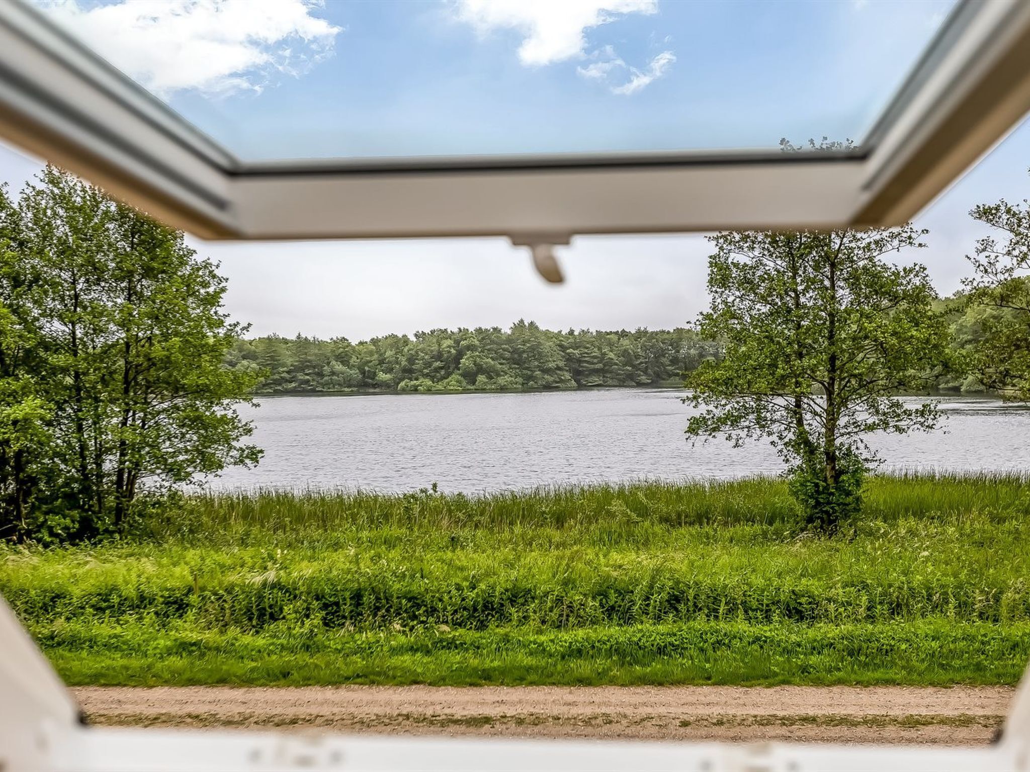 A view from a window overlooking a lake surrounded by trees and grassy areas.