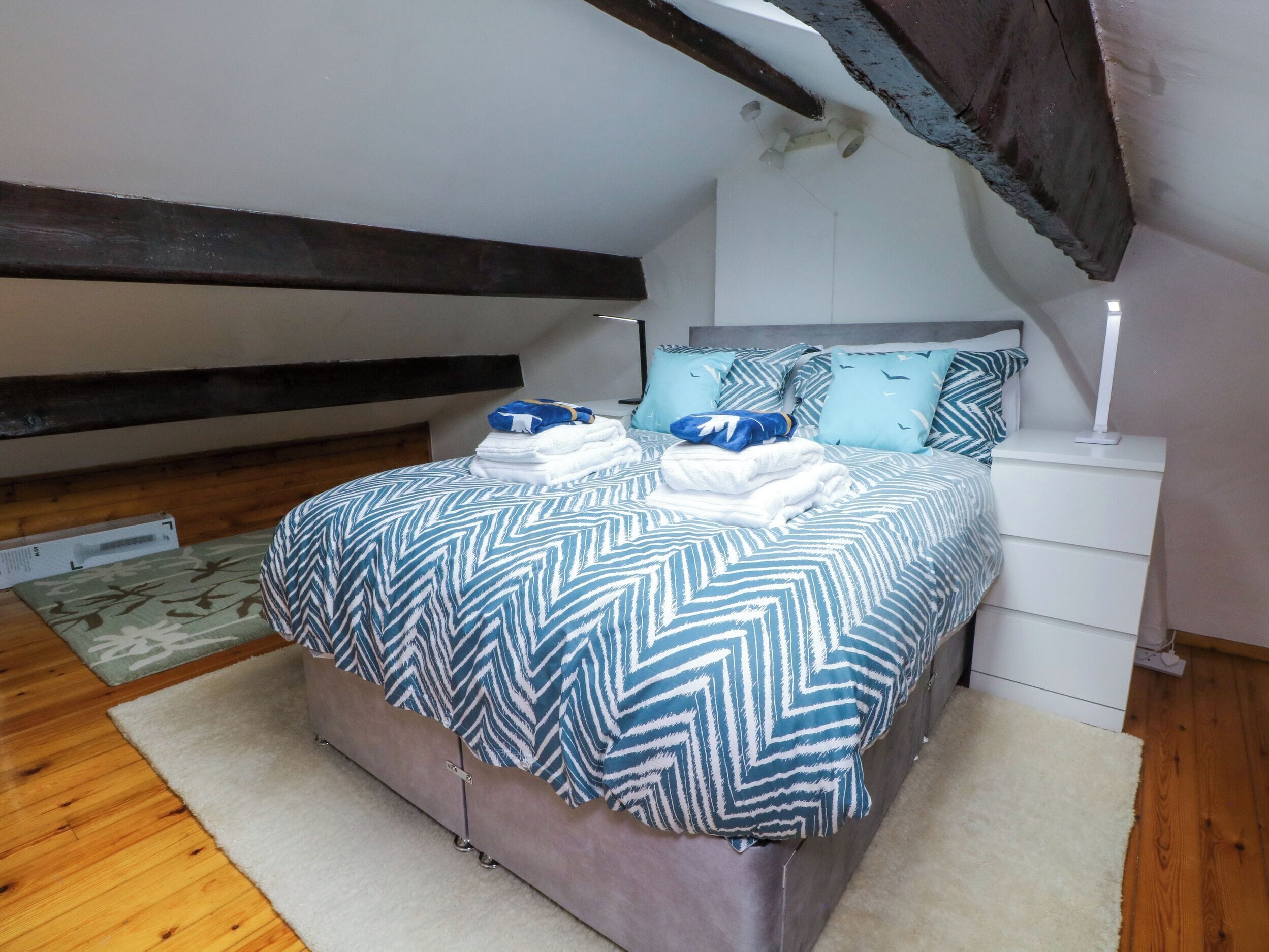 Ein Schlafzimmer mit einem Bett, einem Nachttisch, einer Lampe und Holzboden.