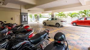A covered parking area with motorcycles and cars, a fire extinguisher, and a visible H sign on the wall. - Housr 50 Luxury Rooms Near Cyber Tower (Hyderabad)