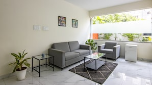 A modern living room with a grey sofa, a glass coffee table, and a small side table. There is a potted plant and a white cabinet. - Housr 50 Luxury Rooms Near Cyber Tower (Hyderabad)