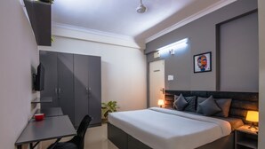 A modern hotel room with a bed, bedside table, lamp, desk, chair, wardrobe, and a small plant. - Housr 50 Luxury Rooms Near Cyber Tower (Hyderabad)