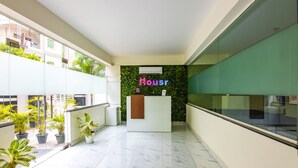 A modern hotel lobby with a reception desk, potted plants, and a green wall with the word "Housr" on it. - Housr 50 Luxury Rooms Near Cyber Tower (Hyderabad)