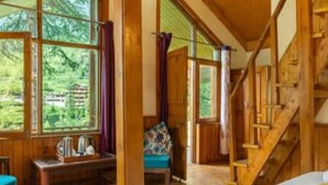 Una cabaña de madera con un ventanal grande, una escalera y una zona de estar acogedora.