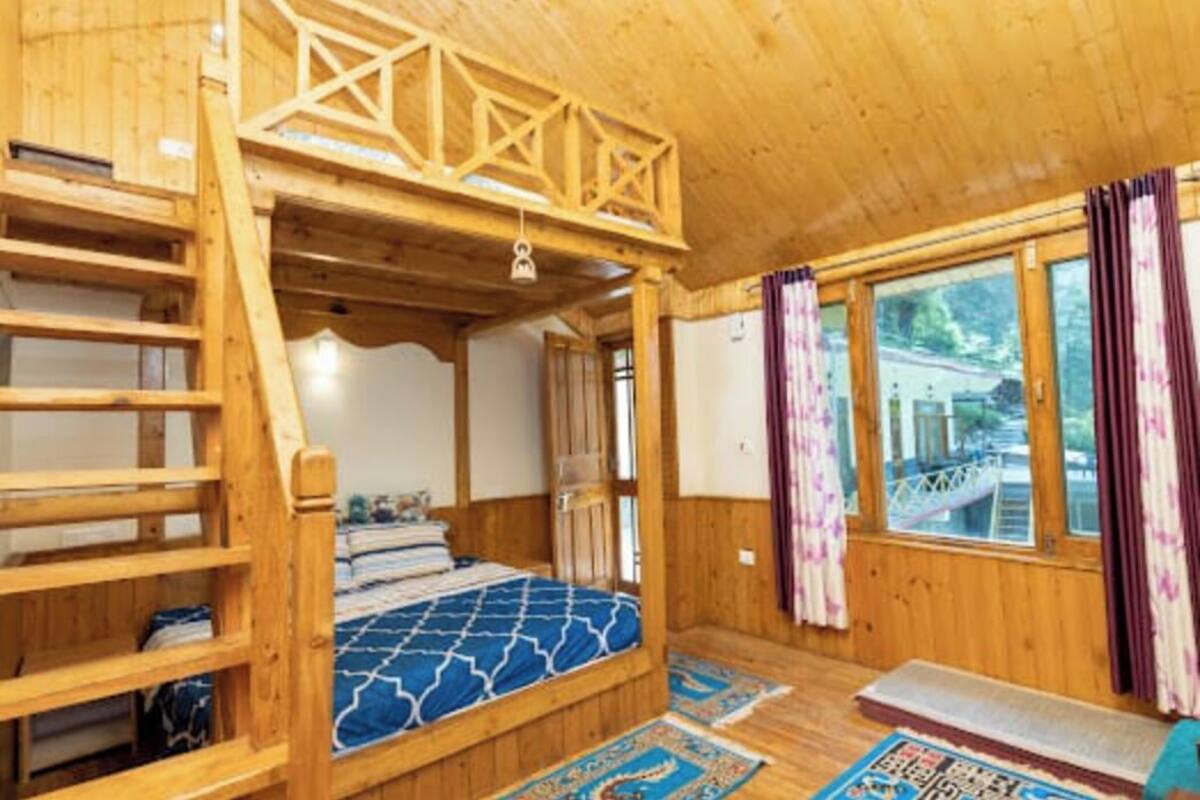 A wooden cabin with a bunk bed, a loft bed, and a window with curtains.