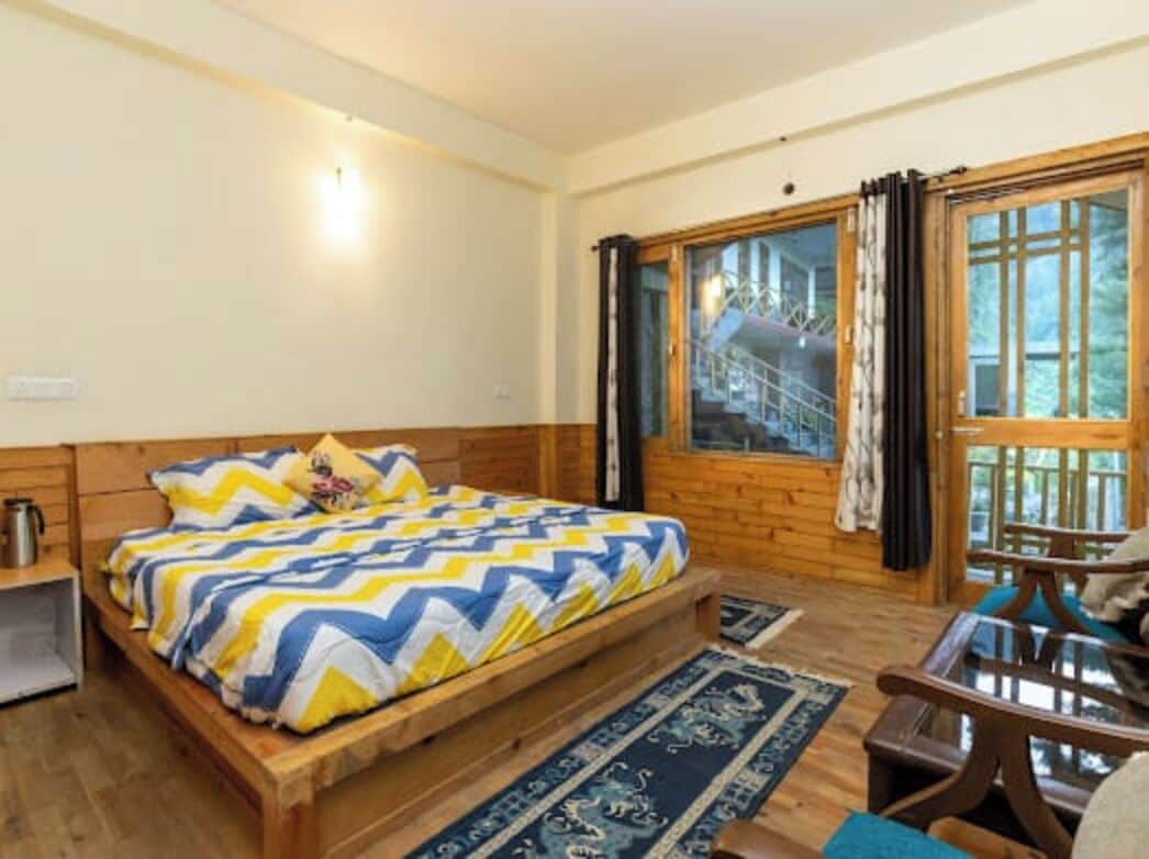 A wooden-framed room with a bed, a small table, and a window with curtains.