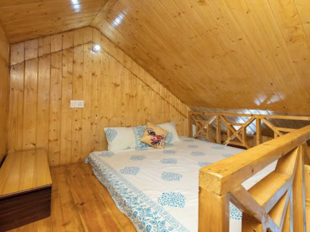 A wooden cabin room with a bed, a bench, and a sloped ceiling.
