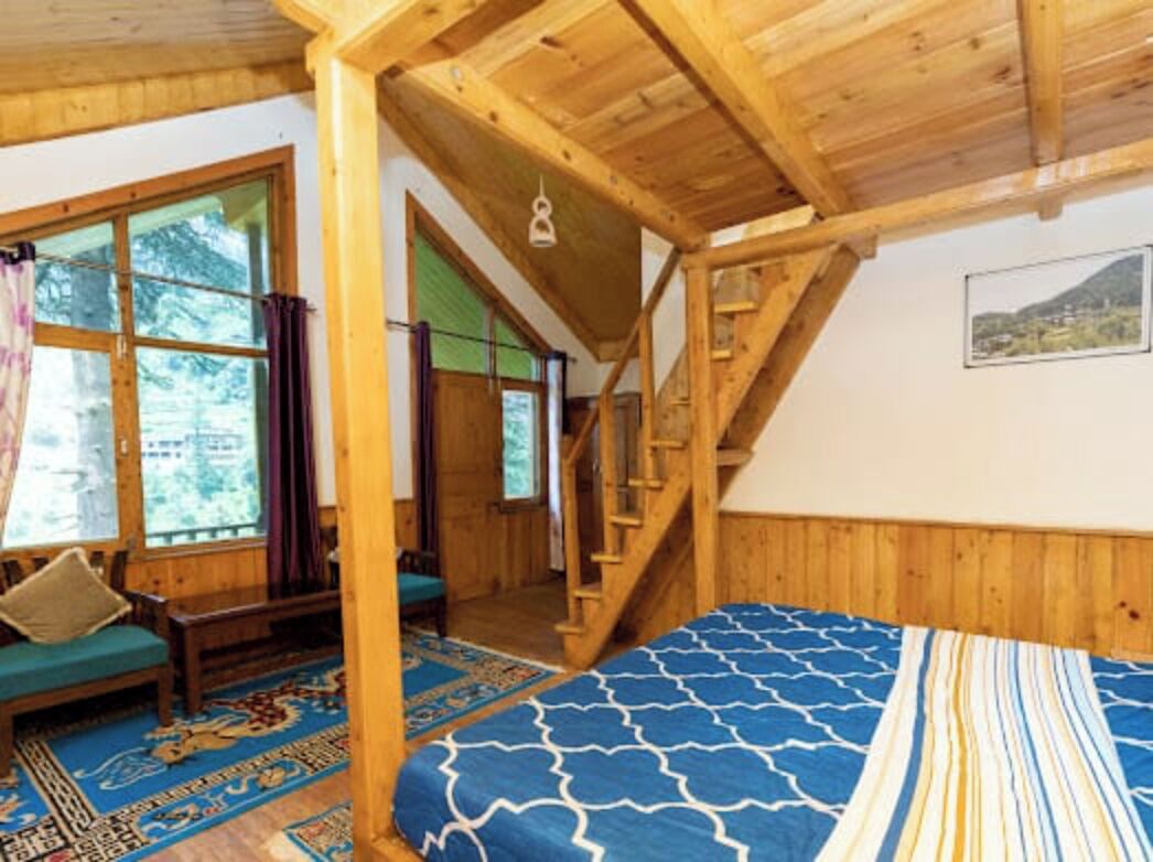 L’intérieur d’un chalet en bois, avec un lit, un canapé, un escalier et de grandes fenêtres.