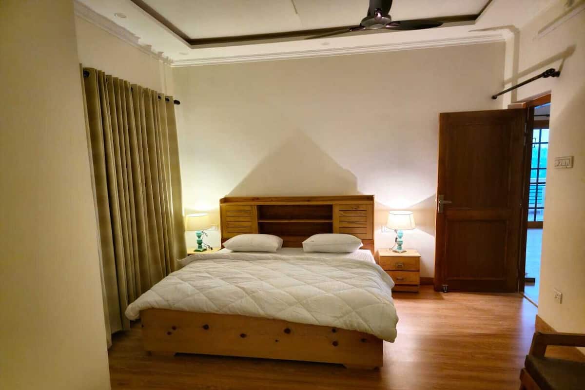 A bedroom with a wooden bed, two bedside tables with lamps, a wooden wardrobe, and a window with curtains.