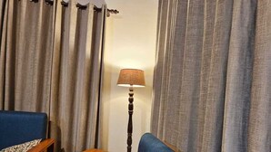 A cozy living room with a blue sofa, wooden side tables, and a lamp. - Laspa Cottage (Bhimtal)