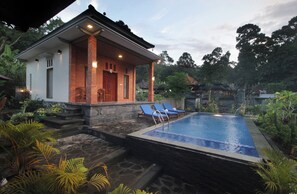 A poolside area with a small building, two blue lounge chairs, and a stone pathway leading to the pool.