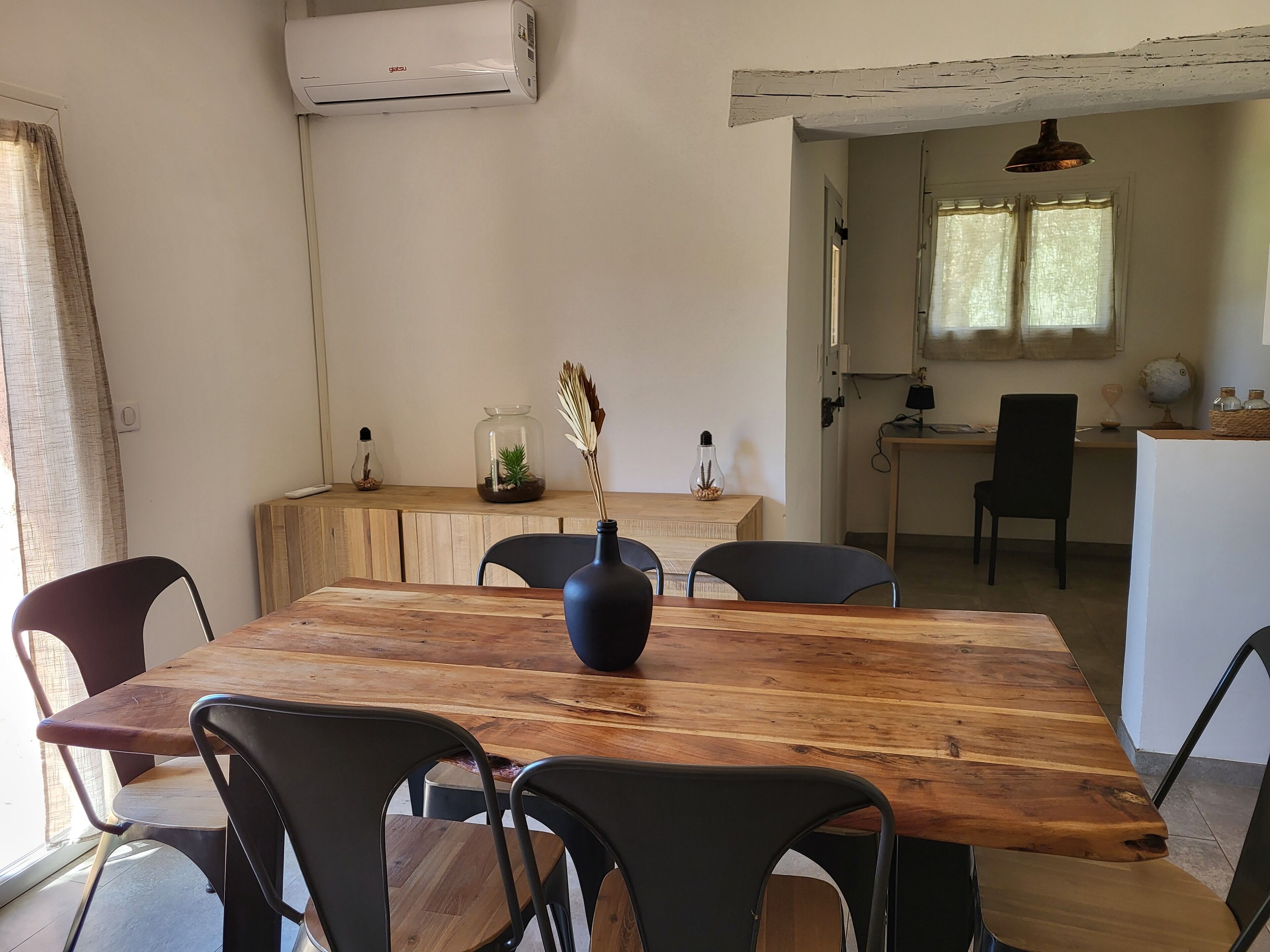 Un coin repas avec une table en bois, des chaises noires et un vase contenant des plantes séchées.