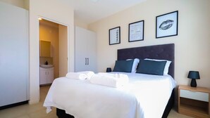 Habitación de hotel con cama, mesita de noche, armario y baño visible a través de una puerta abierta.