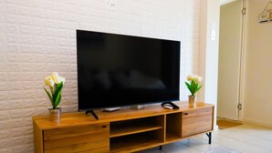 Un televisor de pantalla plana sobre un mueble de madera con dos jarrones, frente a una pared de ladrillo blanco.