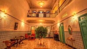 Ein traditionelles marokkanisches Interieur mit aufwendigen Fliesenarbeiten, einer zentralen Sitzgruppe und einem Balkon mit Blick.