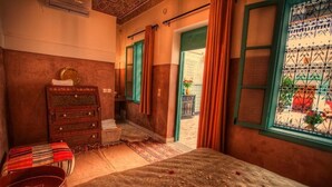 Ein traditionell eingerichtetes Zimmer mit einem Bett, einer Holzkistenkommode und Blick durch ein Fenster mit einem Metallgitter.