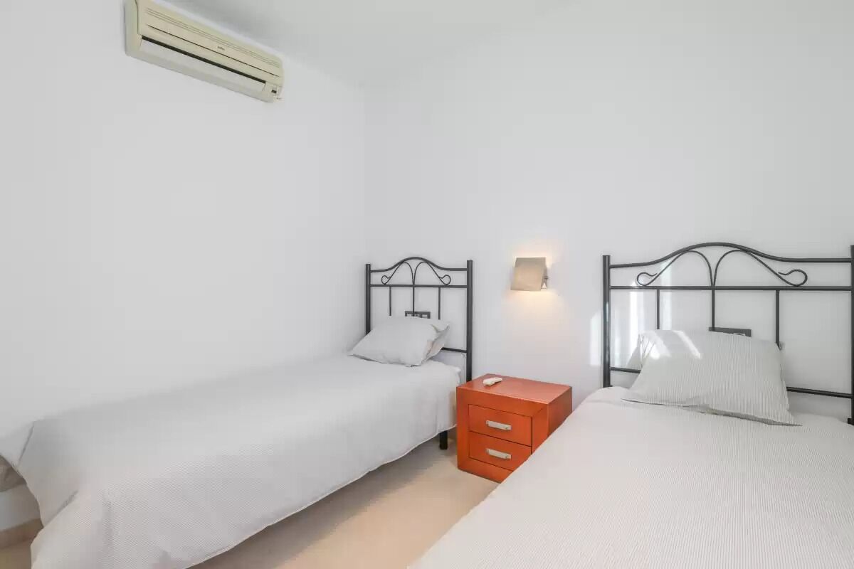 Una habitación con dos camas, una mesita de noche roja pequeña y un aire acondicionado instalado en la pared.