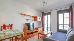 A modern living room with a sofa, TV, wooden furniture, and a balcony with curtains. - Center: 1 room (Dos Hermanas)