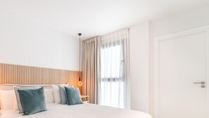 Una habitación de hotel con cama, almohadas, mesita de noche, lámpara y puerta.