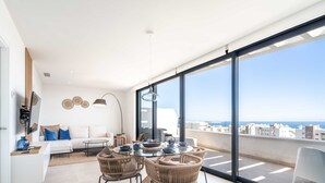 Una sala de estar moderna con un gran ventanal, un comedor con sillas de mimbre y un sofá blanco.