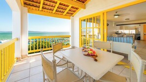 Ein Balkon mit Meerblick, ein Essbereich mit Tisch für zwei Personen und eine durchgehende Tür sichtbare Küche.