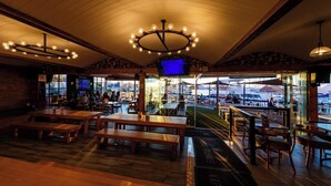 Ein Restaurant mit Holztischen und -bänken, einem Fernsehbildschirm und Blick auf Boote.