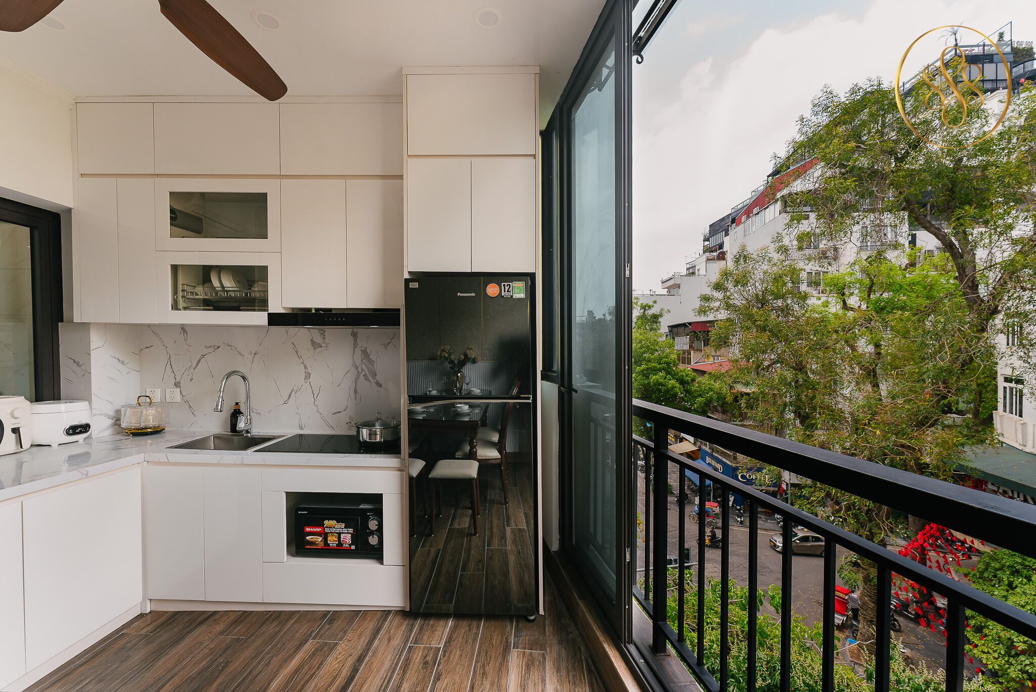 Une cuisine moderne avec des meubles blancs, un réfrigérateur noir et une vue sur la ville grâce à de grandes fenêtres.