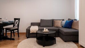 Un salon moderne avec un canapé gris, une table basse ronde, un fauteuil noir et une table à manger avec des assiettes et un verre à vin.
