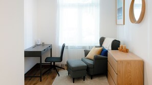Quarto moderno e bem iluminado, com escrivaninha, cadeira, banquinho e cômoda.