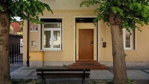 Un bâtiment avec une porte en bois, un banc et un arbre devant.