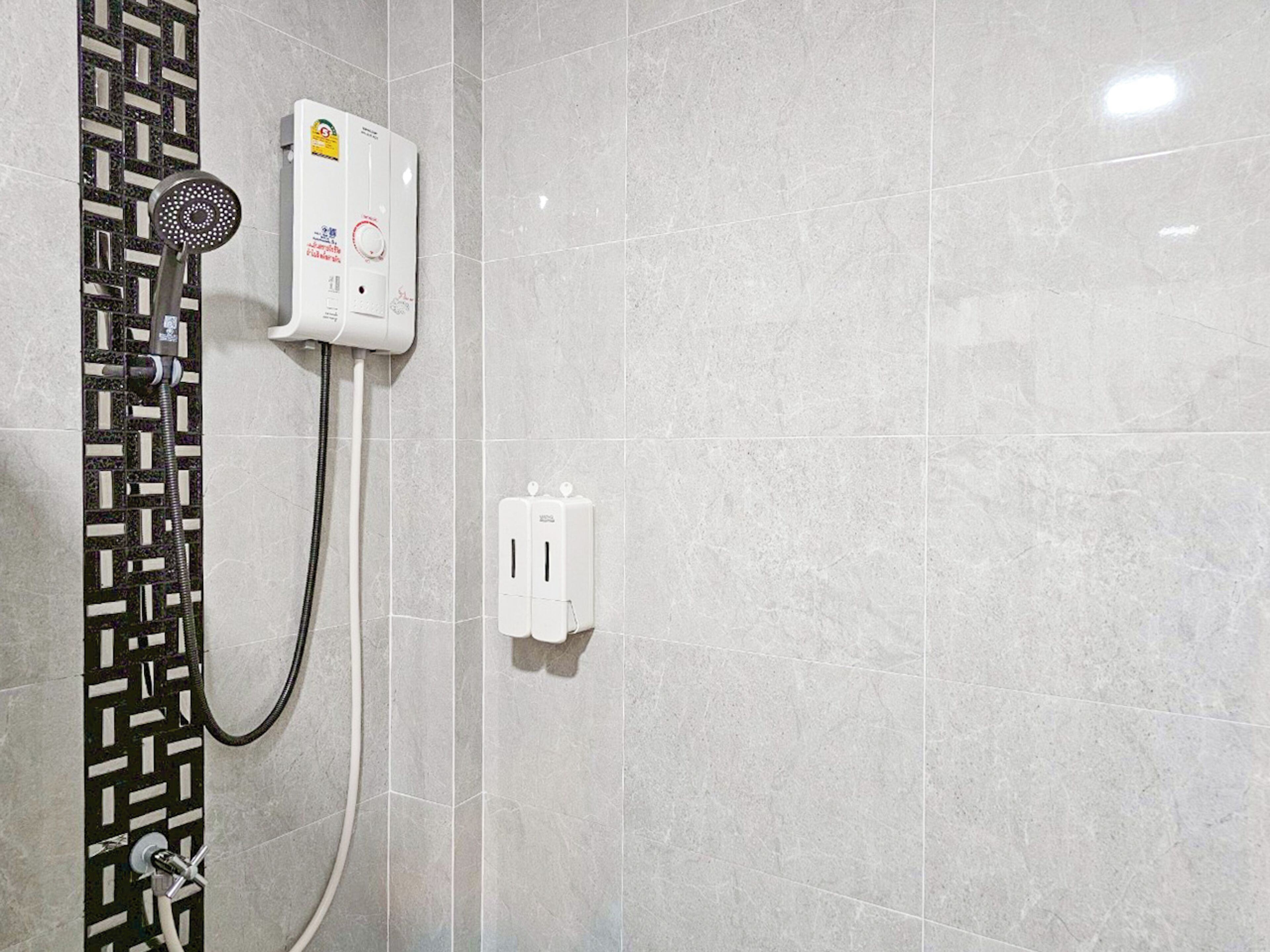 A shower with a handheld showerhead, a control panel, and a power outlet on a tiled wall.