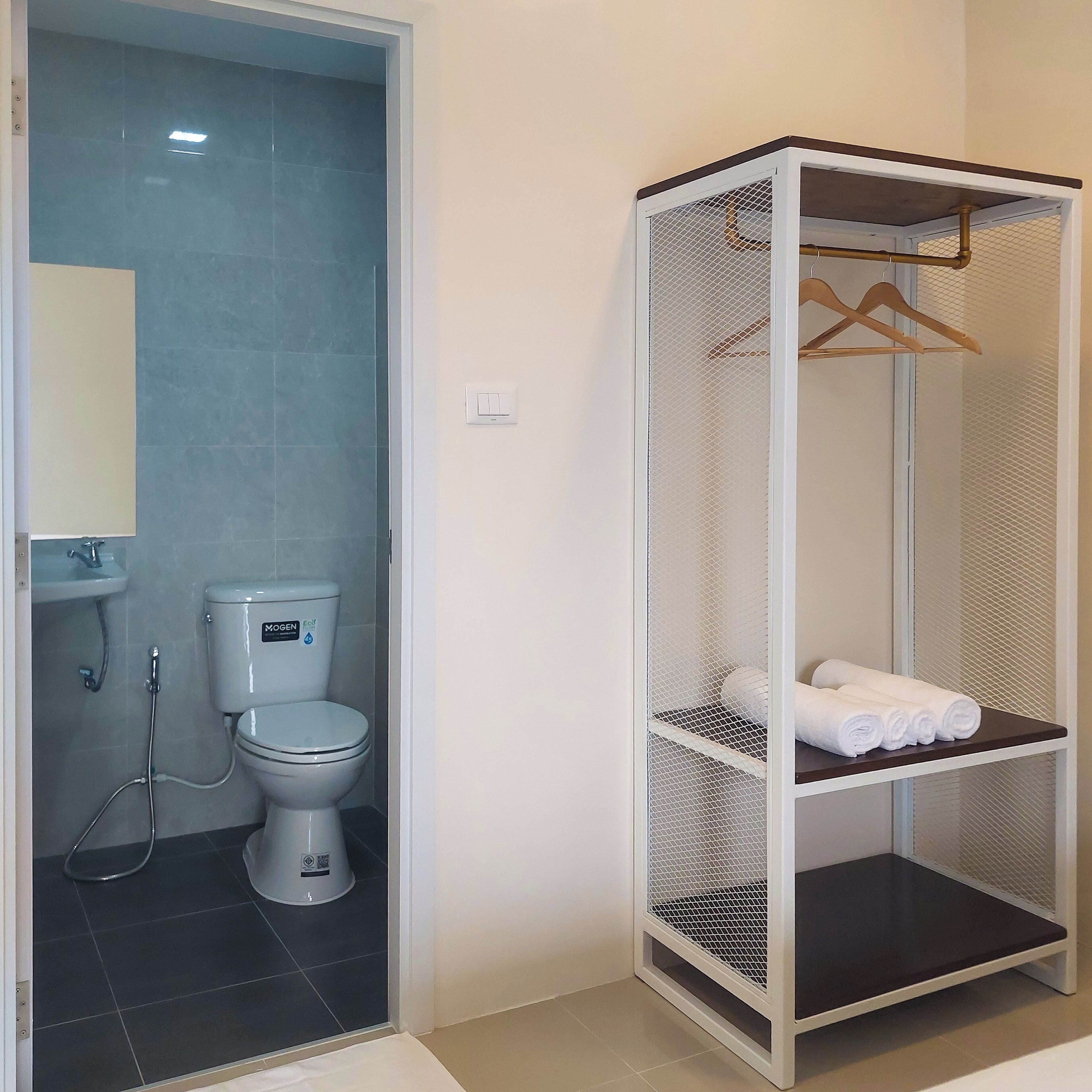 Een badkamer met toilet, wastafel en een inloopkast met hangende kleding.