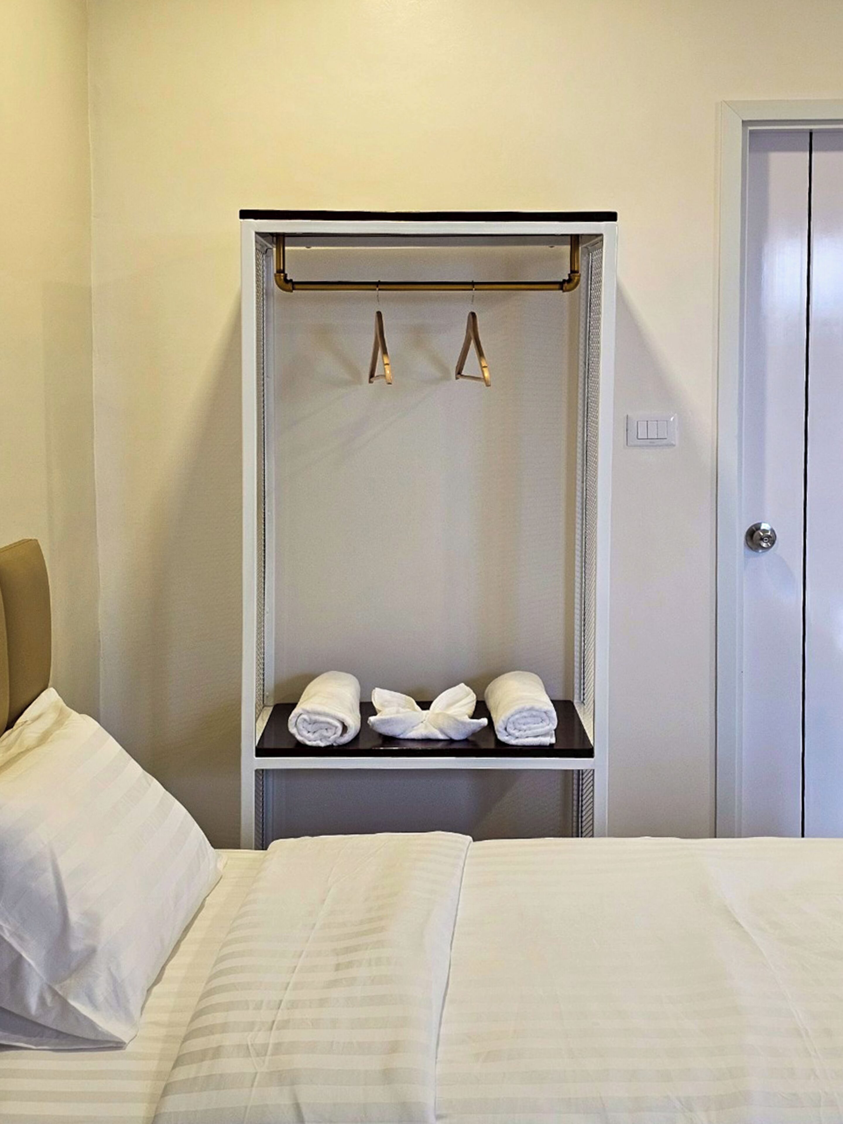 Une chambre d’hôtel avec un lit, une armoire et une étagère où sont rangées les serviettes.