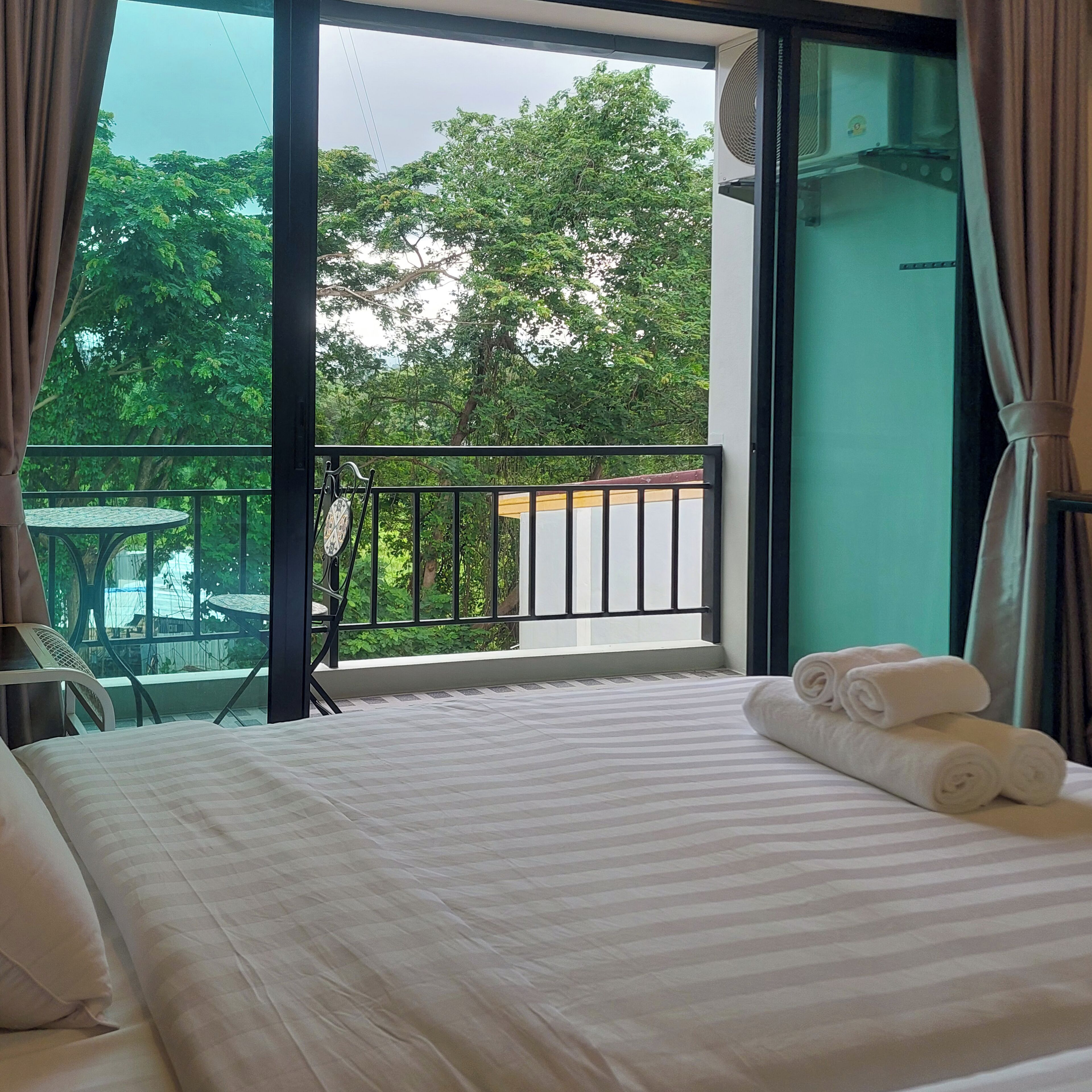 A hotel room with a large bed, a balcony with a table and chairs, and a view of trees.