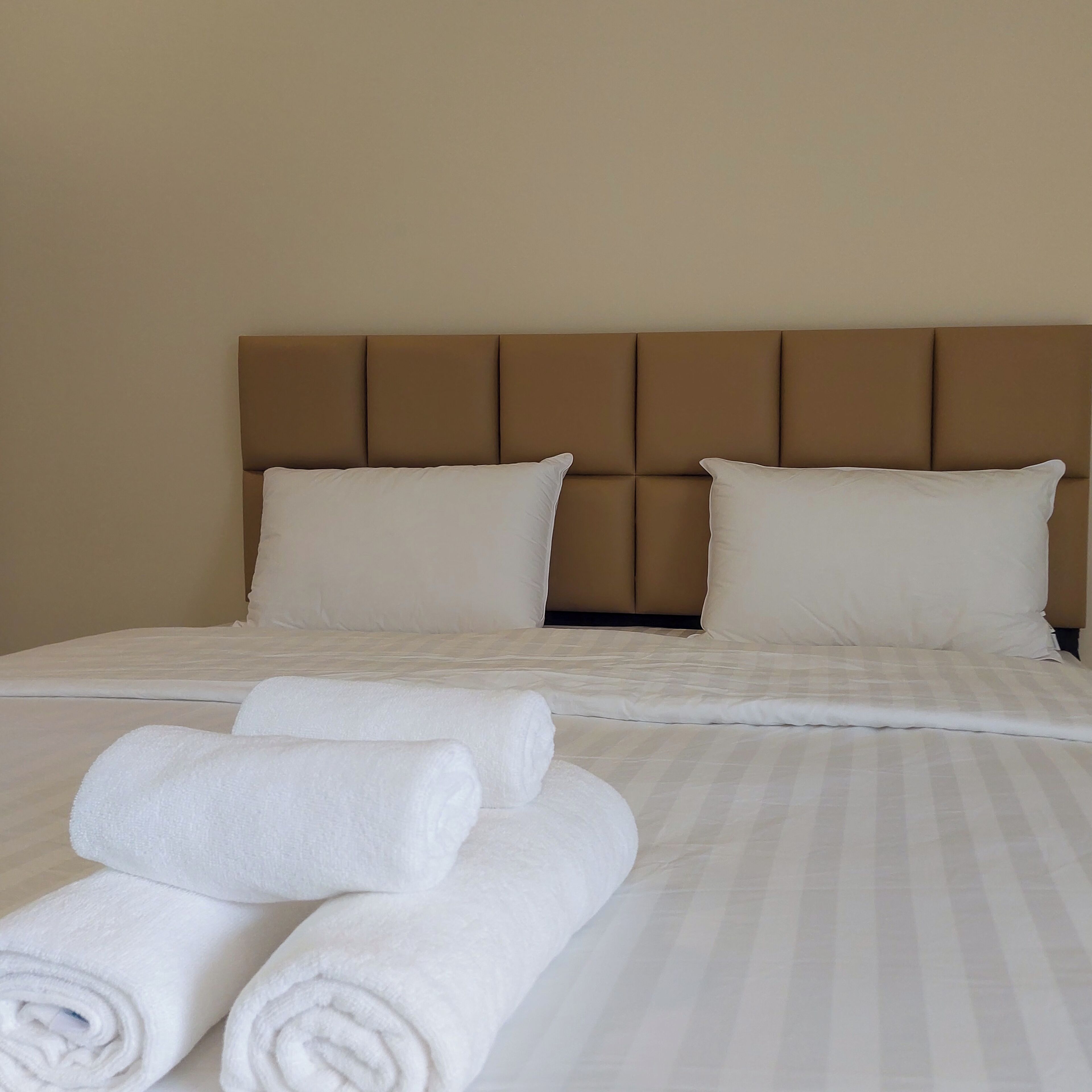 A neatly made bed with a headboard, two pillows, and rolled towels.