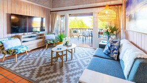Un salon confortable avec une grande télévision, un canapé, une table basse et un balcon aménagé avec du mobilier d’extérieur.