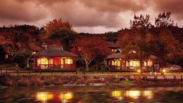 Un chalet au bord du lac composé de deux bâtiments principaux, chacun doté d’un porche abrité et d’une cheminée centrale.