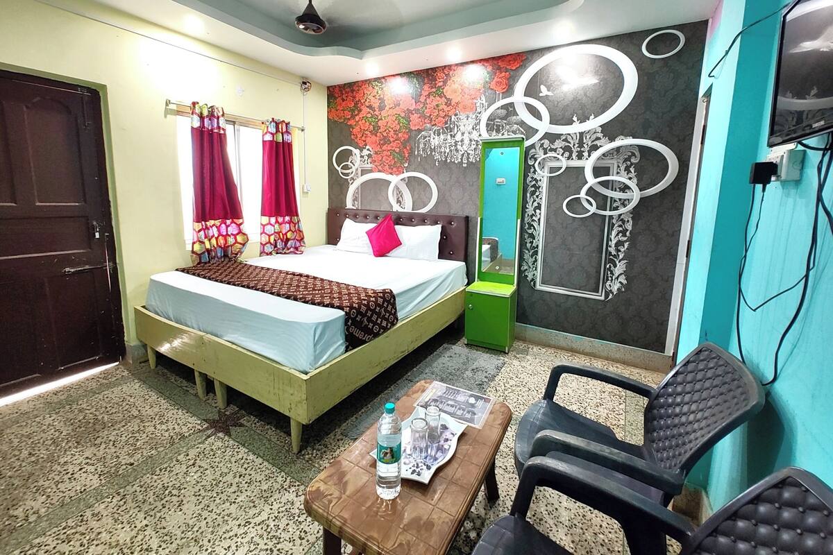 A bedroom with a bed, a mirror, a table with a bottle and glasses, and a chair.