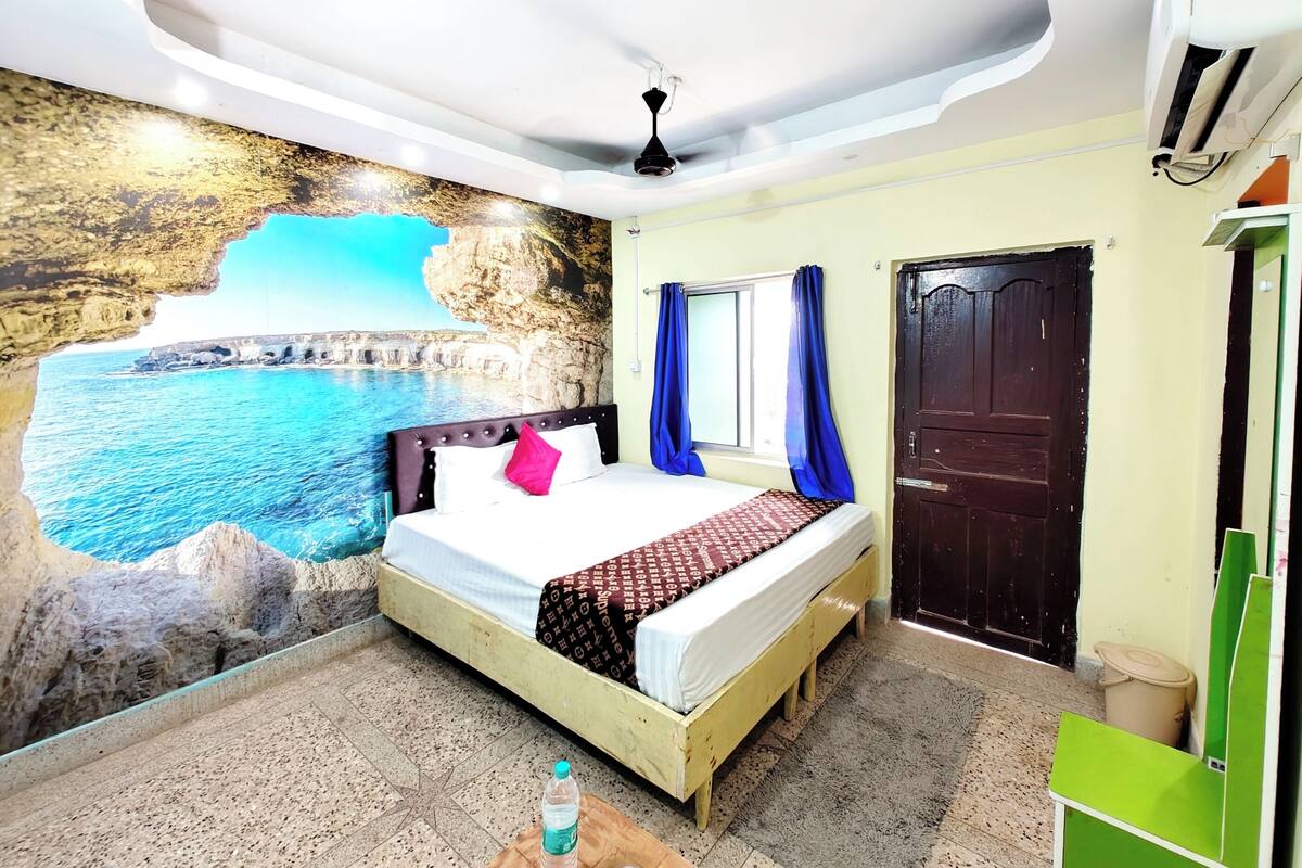 A bedroom with a bed, a wall mural of a coastal scene, a ceiling fan, and a door.