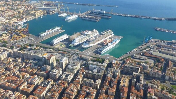 An aerial view of a coastal city with a marina, including several cruise ships docked and a prominent bridge in the background. - UN PASSO DAL PORTO (Palermo)