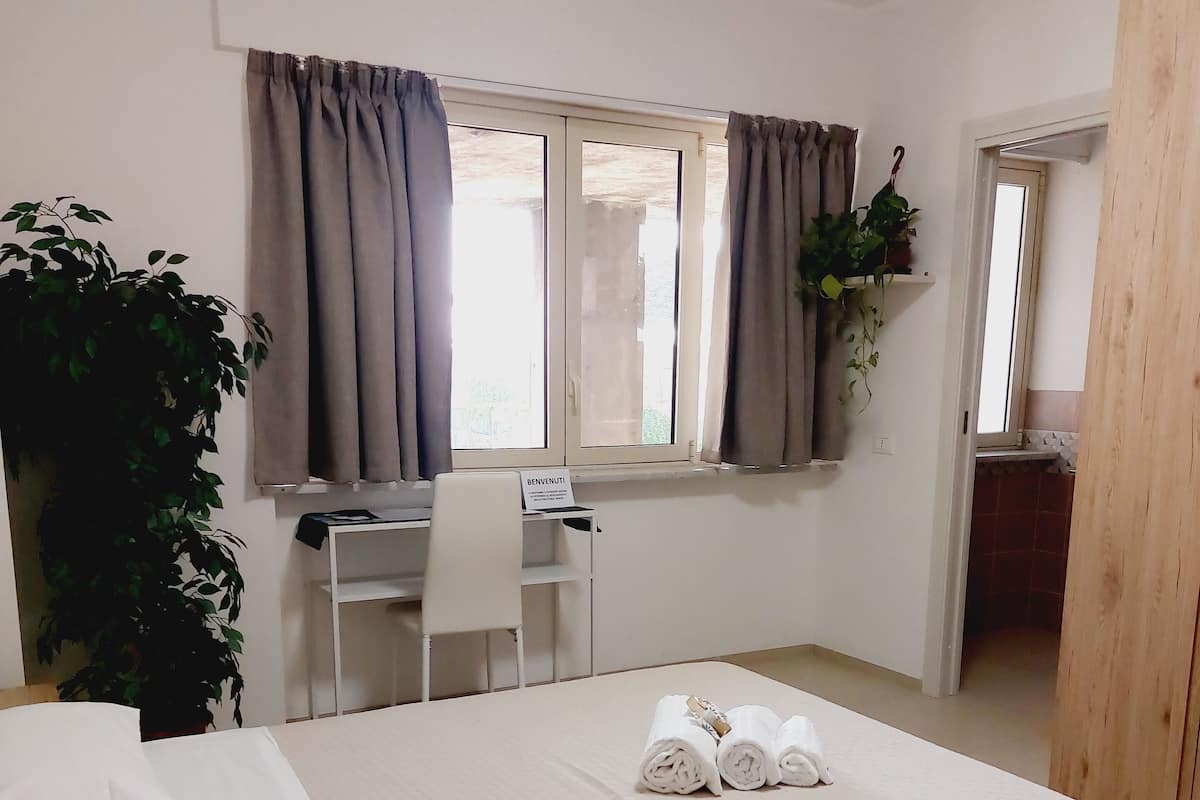 A hotel room with a bed, a desk, and a chair. There is a sign on the desk that says "BENVENUTI".