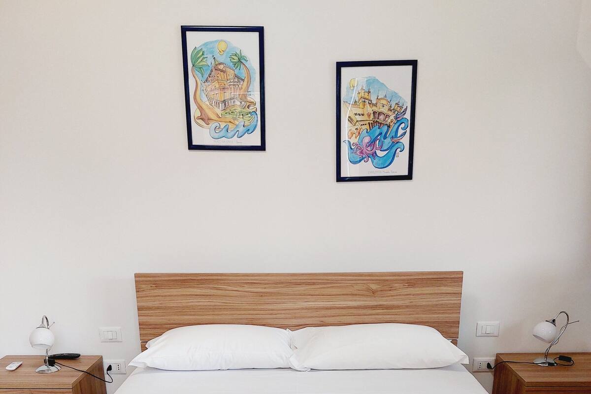 A neatly made bed with a wooden headboard, two bedside tables with lamps, and two framed artworks on the wall.