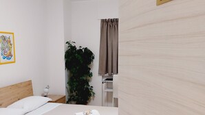 A neatly arranged bedroom with a bed, a bedside table, a potted plant, and a window with curtains. - UN PASSO DAL PORTO (Palermo)