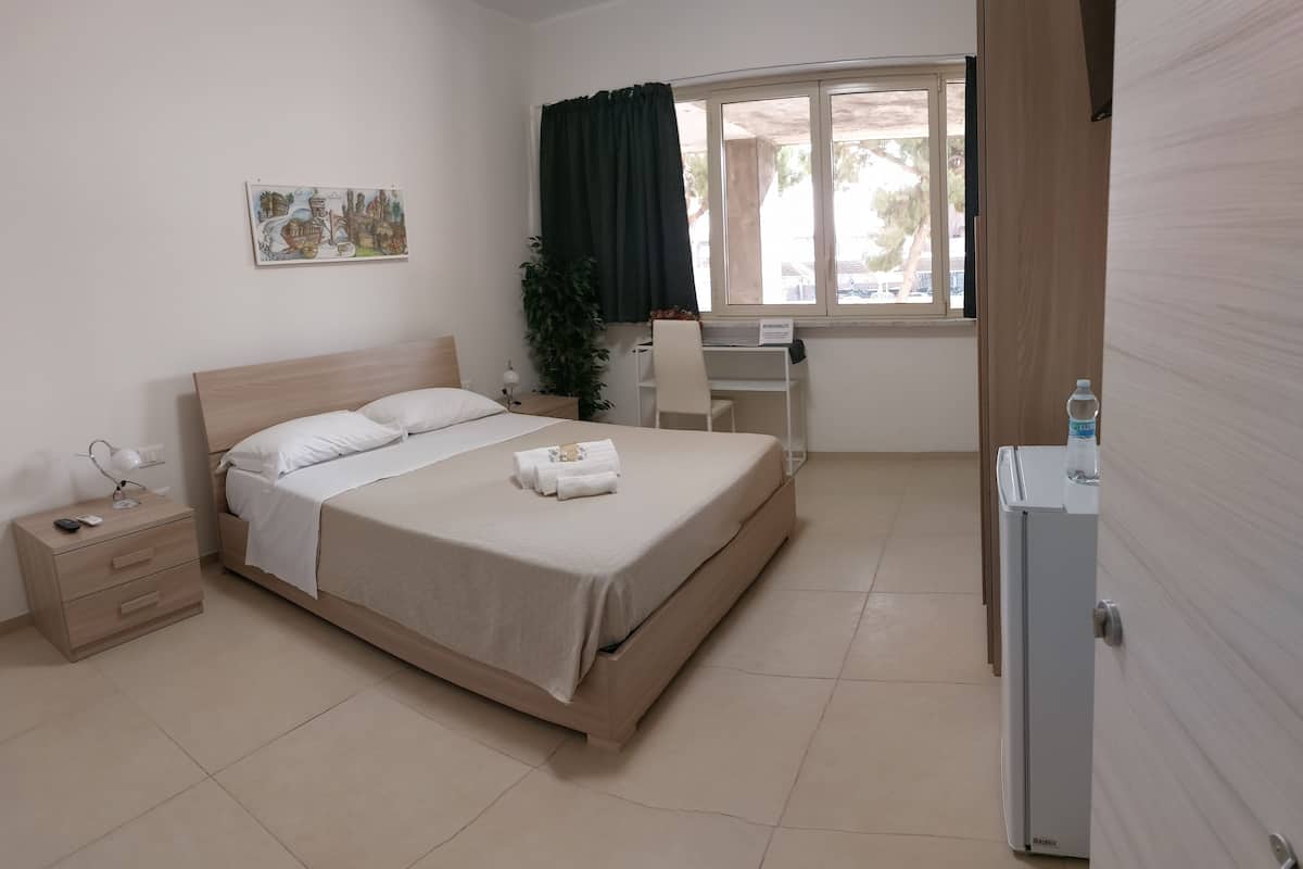 A neatly arranged bedroom with a bed, bedside table, desk, chair, and a window with curtains.