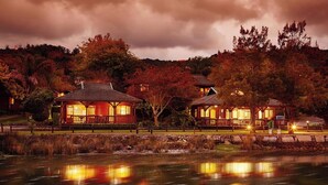 A lakeside lodge with two main buildings, each featuring a covered porch and a central chimney. - Luxury Family Chalet | BBQ Deck & Lagoon View (Knysna)